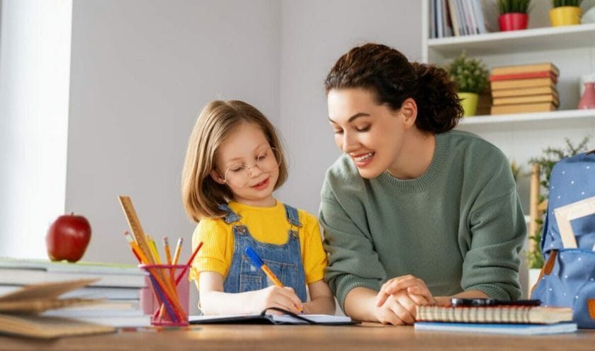 An image of a happy child and her mother sitting at a desk doing homework.