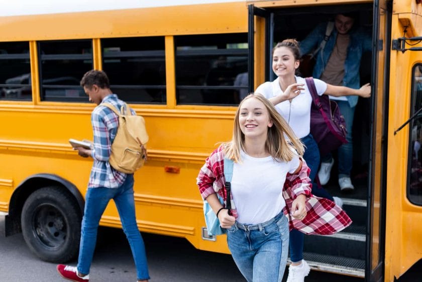 An image of happy multiethnic teen scholars running out school bus.