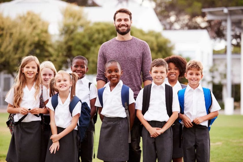 An image of Elementary School Pupils With Teacher Wearing Uniform Standing On Playing Field.