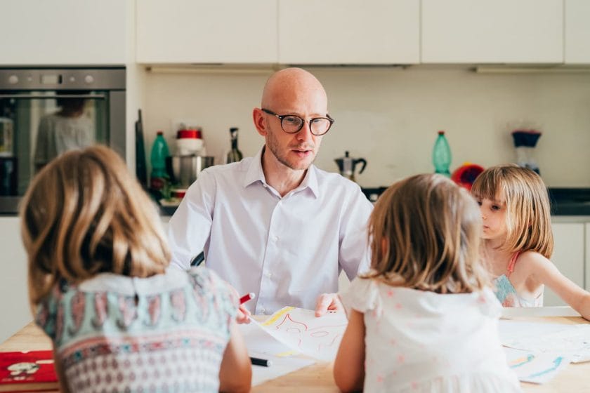 An image of a Father and three children homeschooling indoors - teaching, mentoring, education concept.