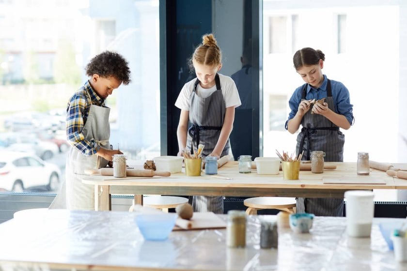 An image of Three creative children standing by the workplace while making things from clay in the workshop.