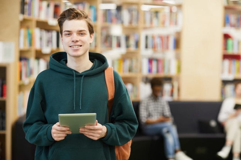 An image of a Cheerful high school student holding a tablet and smiling at the camera.