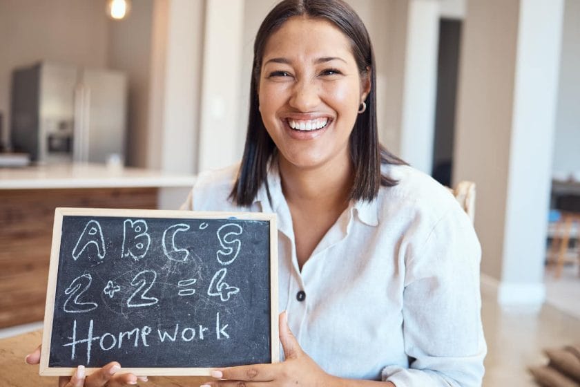 An image of a female teacher holding a blackboard in a homeschooling setup.