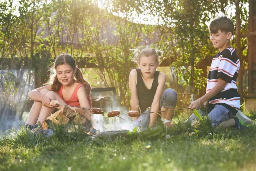 An image of Children enjoying the campfire and toasting sausages in the garden at sunset.