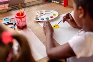 An image of Two little girls sitting at a desk, painting with water colors and having fun while doing homeschooling art class.
