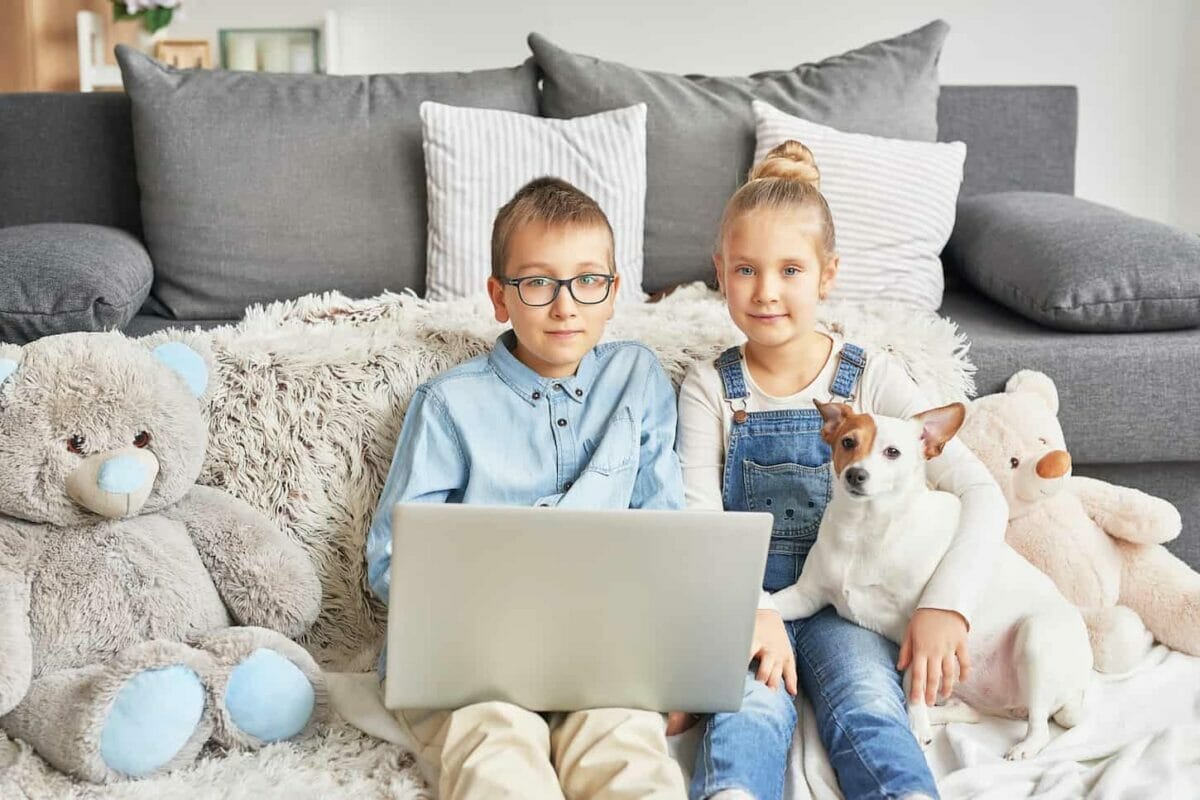 An image of Homeschooler kids holding a dog while doing online interaction at home.