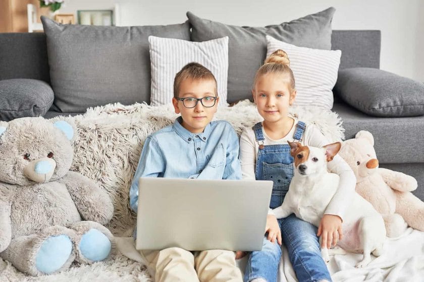An image of Homeschooler kids holding a dog while doing online class interaction at home.