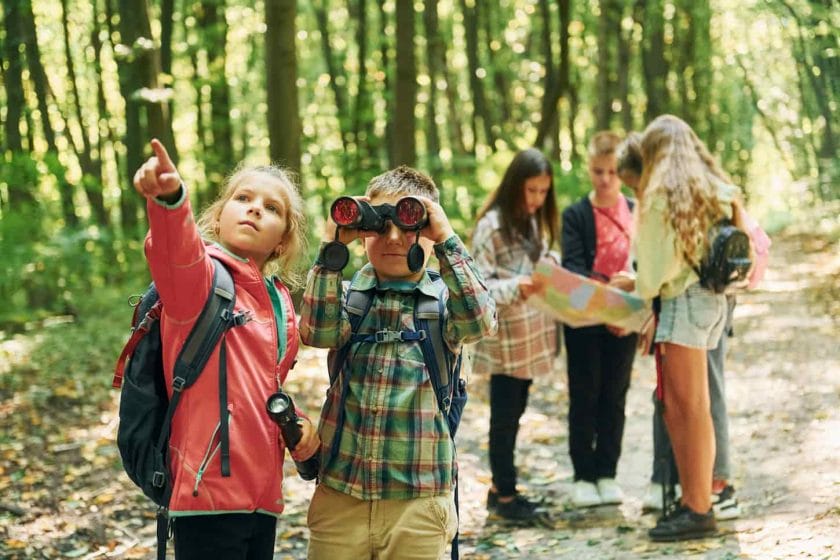 An image of homeschooled kids in a green forest at summer daytime together.