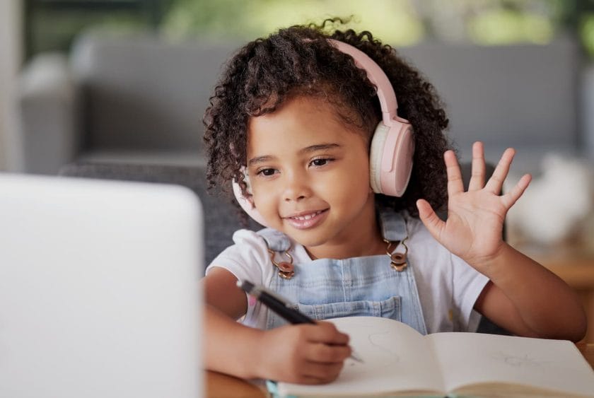 An image of a child in a Video call waving hello in front of the laptop in an online class.